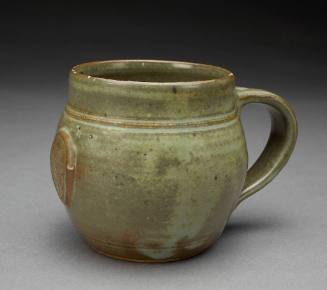 A handcrafted stoneware mug with a greenish-brown glaze and a decorative medallion.