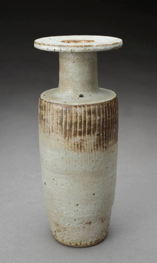 A tall, narrow ceramic vase with a ribbed texture and wide, flat rim.