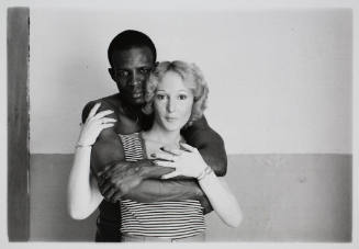 A black-and-white photo of a couple, a dark-skinned man and a light-skinned woman, embracing an…